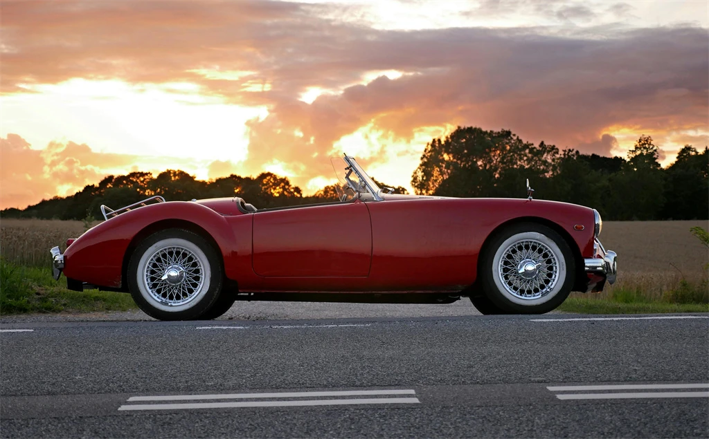 a red convertible sports car parked by the roadside with a brilliant sunset in the background